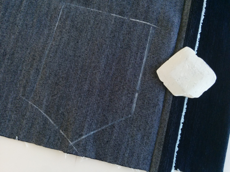A pocket is marked on the bad side of a piece of double-folded denim, ready to be cut good sides together. After cutting both layers, this will yield two pockets that are mirror images of each other.